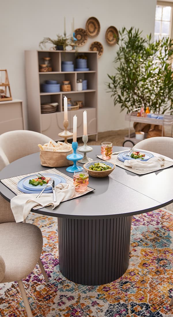 Modern gedeckter Esstisch mit Kerzen, Salat und Brot, dahinter Regal mit Geschirr und Pflanze.