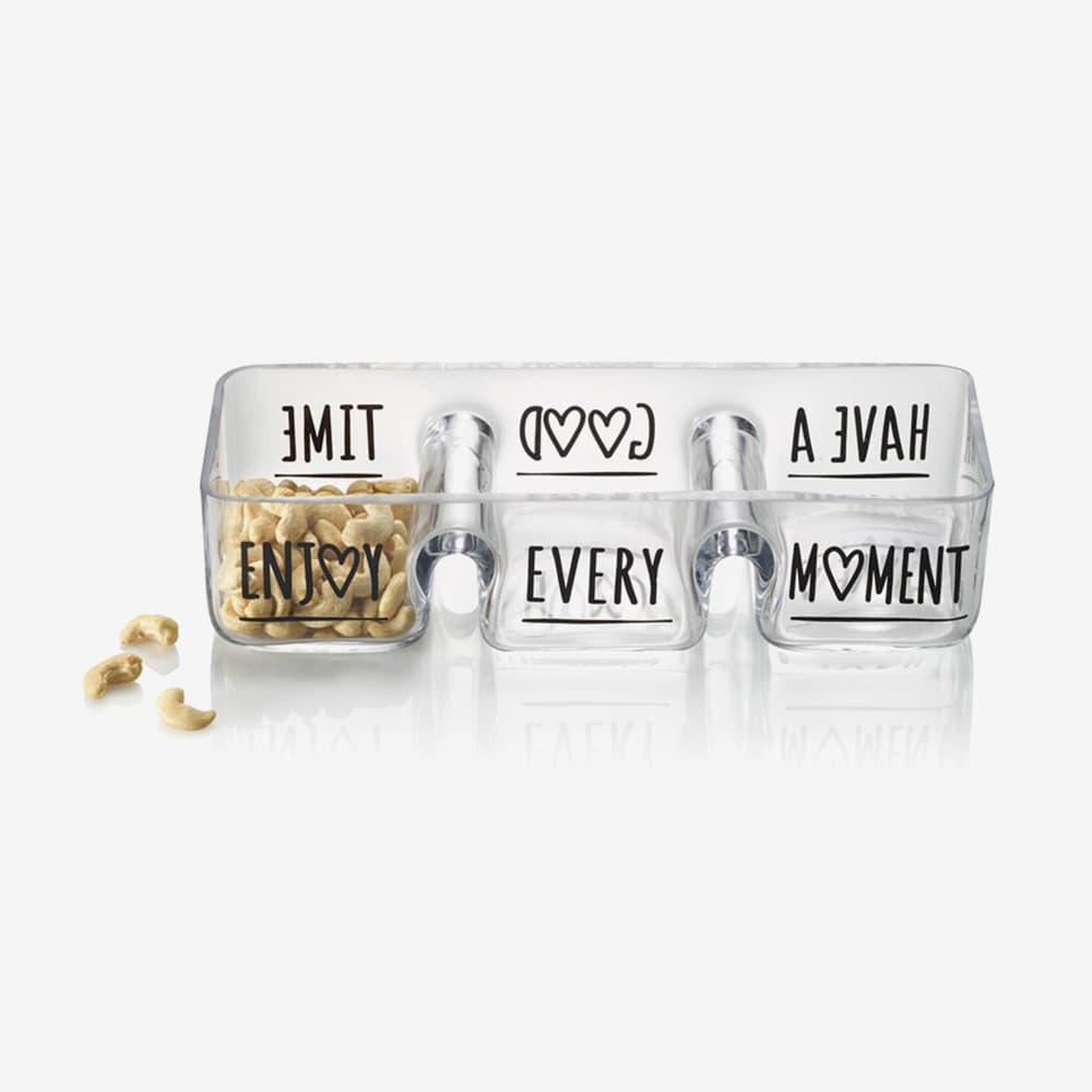 Schale mit den Worten "ENJOY EVERY MOMENT" und Herzsymbolen, gefüllt mit Cashewnüssen, daneben liegen einige Nüsse.