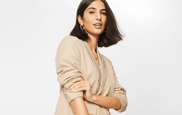 Frau mit schulterlangem Haar trägt beigefarbenen Blazer und hat die Arme verschränkt.
