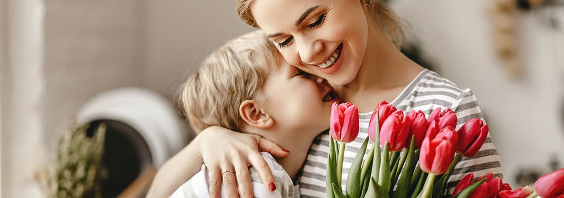 Kind umarmt eine erwachsene Person mit gestreiftem Shirt, im Vordergrund ein Strauß roter Tulpen