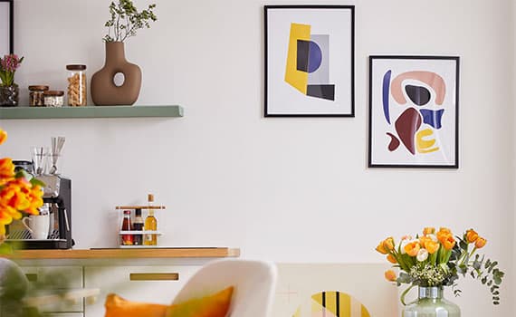 Wohnküche mit abstrakten Wandbildern, Kaffeemaschine auf Arbeitsplatte und Vase mit orangefarbenen Blumen auf Beistelltisch