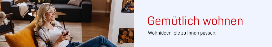 Gemütlich wohnen – Frau sitzt entspannt im Sessel mit Getränk, im Hintergrund Sofa und Kamin im Wohnzimmer