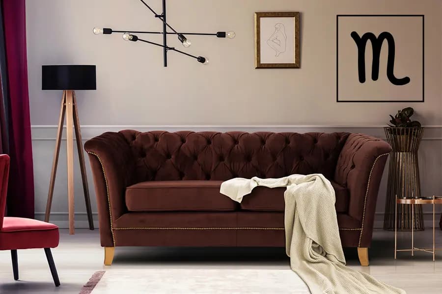 Braunes Sofa mit gesteppter Rückenlehne, cremefarbene Decke darauf, moderne Lampe und Wandbilder im Hintergrund.