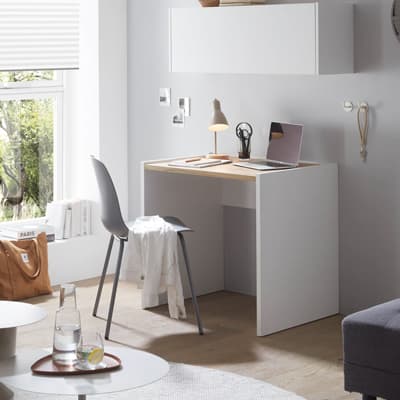 Kompakter Schreibtisch mit Laptop und Lampe in hellem Raum, grauer Stuhl mit weißem Hemd, Tasche auf dem Boden, Fenster links