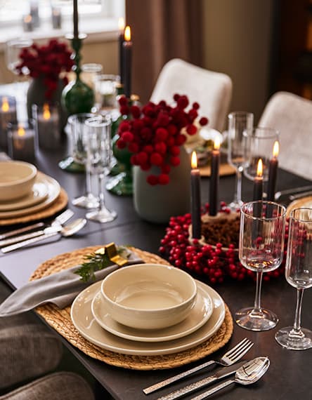 Festlich gedeckter Tisch mit Kerzen, roten Beeren und Geschirr, Besteck und Gläsern auf runden Platzsets