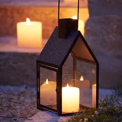 Beleuchtete Laterne mit Kerze im Vordergrund, weitere Kerzen auf Stufen im Hintergrund, Nachtaufnahme