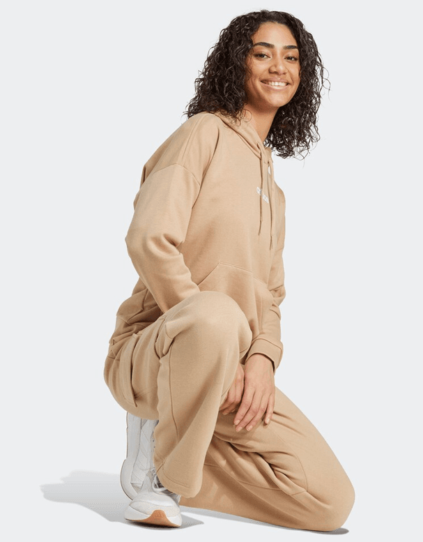 Personne accroupie portant un ensemble beige avec un sweat à capuche et un pantalon large, chaussures blanches.