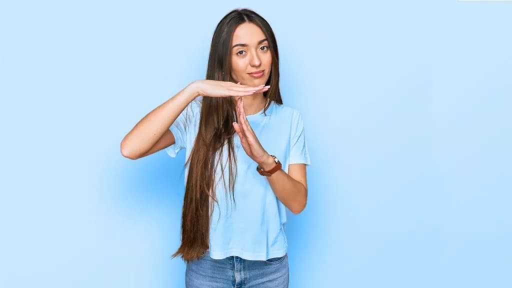 Frau in hellblauem T-Shirt zeigt Handzeichen für Pause vor hellblauem Hintergrund
