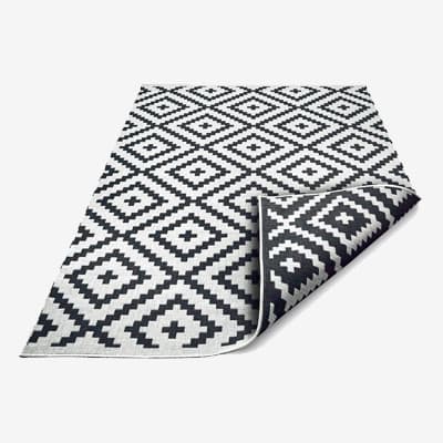 Teppich mit schwarz-weißem Rautenmuster, eine Ecke ist nach vorne umgeschlagen