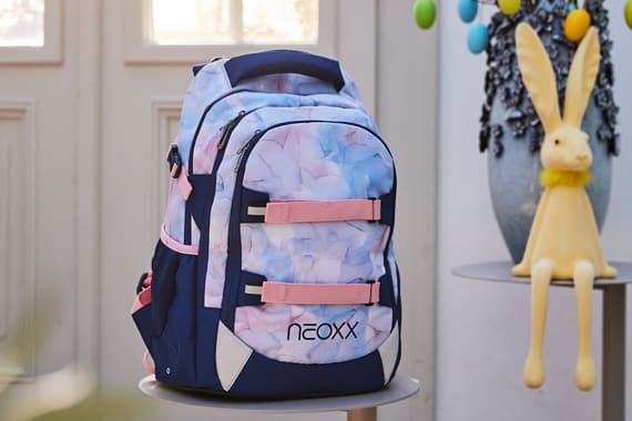 Rucksack mit rosa-blauem Muster auf einem Tisch, daneben eine gelbe Hasenfigur auf einem weiteren Tisch.