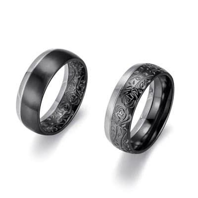 Zwei dunkle Ringe, einer glatt, einer mit feinen floralen Ornamenten, schwebend vor weißem Hintergrund