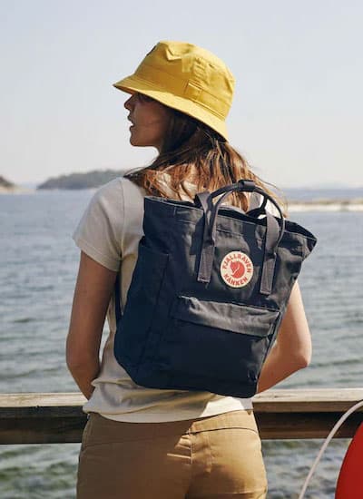 Beiger rechteckiger Rucksack mit Tragegriffen oben, Fronttasche und rundem Fjällräven Kånken Logo vorne