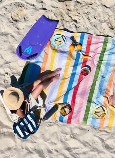 Bunte Picknickdecke mit bunten Längsstreifen, daneben passender Beutel mit Aufdruck „Picnic Blanket“