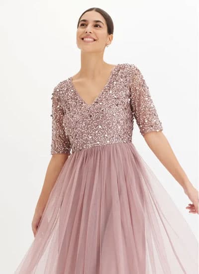 Frau in roséfarbenem Abendkleid mit Paillettenoberteil und schwingendem Tüllrock vor hellem Hintergrund