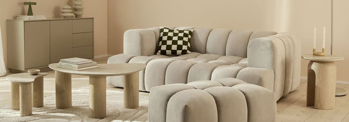 Beiges Wohnzimmer mit modularem Sofa und Hocker, kariertem Kissen, runden Holztischen, Sideboard und Stehlampe