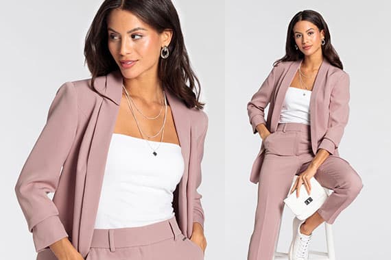 Frau in rosafarbenem Hosenanzug und weißem Top, sitzt auf Hocker und hält weiße Clutch in der Hand