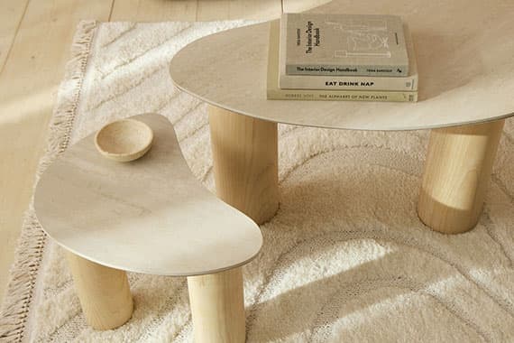 Zwei organisch geformte Couchtische auf hellem Teppich, darauf Bücher und eine kleine Schale