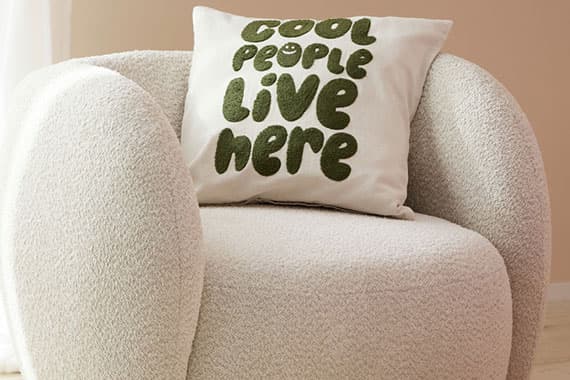 Cool people live here – quadratisches Zierkissen mit Schrift auf rundem, hellen Sessel
