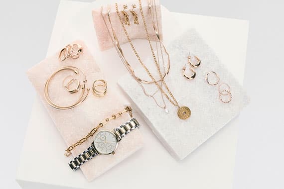 Frau mit langen Haaren trägt mehrere Halsketten, lange Ohrhänger, Armband und Ring zu weißer Bluse