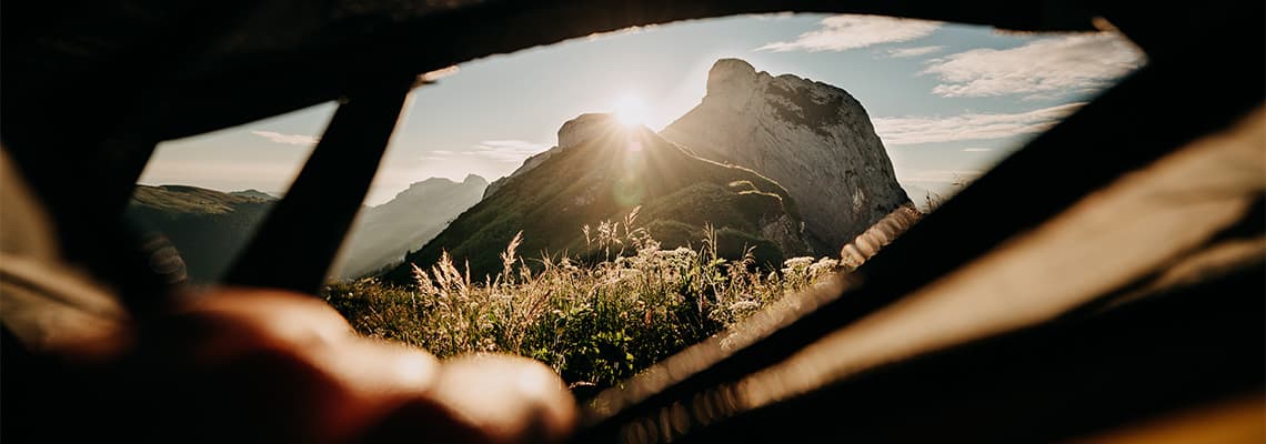 Lever de soleil sur une montagne verdoyante, vue depuis l’ouverture d’une tente de camping