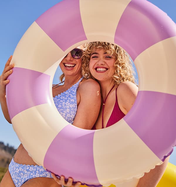 Zwei Frauen in Bikinis schauen durch einen großen, gestreiften Schwimmring in die Kamera