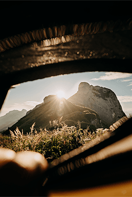 Sonnenaufgang hinter einem Berggipfel, betrachtet durch einen Fahrzeugrahmen mit unscharfer Hand im Vordergrund