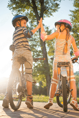 Zwei Kinder mit Helmen geben sich auf ihren Fahrrädern ein High-Five in der Sonne