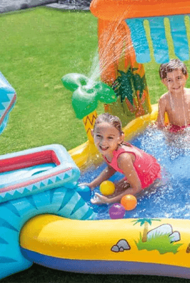 Kinder spielen mit bunten Bällen in einem aufblasbaren Wasserspielplatz mit Rutsche und Fontäne im Garten