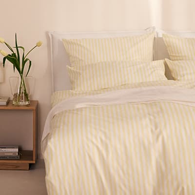 Bett mit gelb gestreifter Bettwäsche, auf dem Nachttisch Glasvase mit Tulpen und Bücher in einem hellen Schlafzimmer