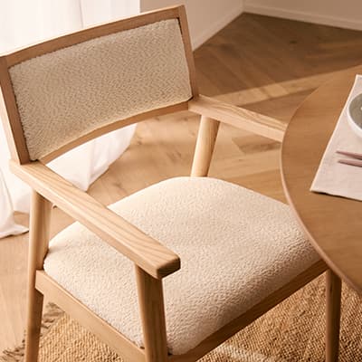 Heller Esszimmerstuhl mit gepolsterter Sitzfläche und Rückenlehne neben rundem Holztisch auf Parkettboden