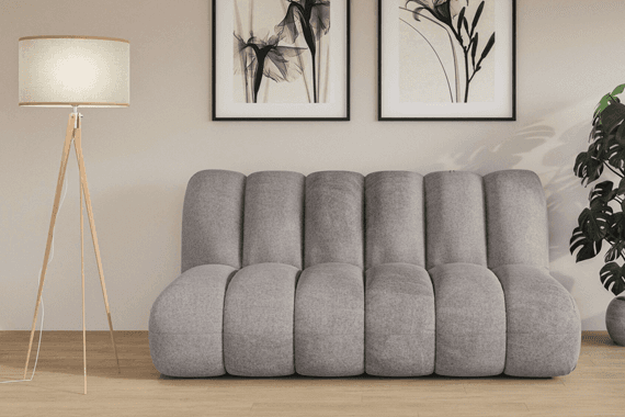 Canapé gris à larges coussins dans un salon épuré, avec lampadaire sur trépied et deux tableaux abstraits au mur