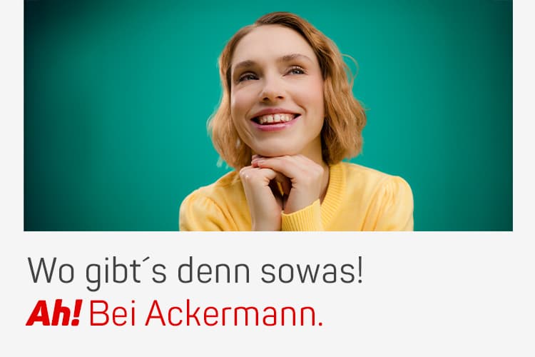 Wo gibt’s denn sowas! Ah! Bei Ackermann. Frau in gelbem Pullover lächelt mit gestütztem Kinn vor grünem Hintergrund