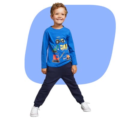 Junge in blauem Langarmshirt mit Fahrzeugmotiv und dunkler Hose steht breitbeinig und lächelt in die Kamera