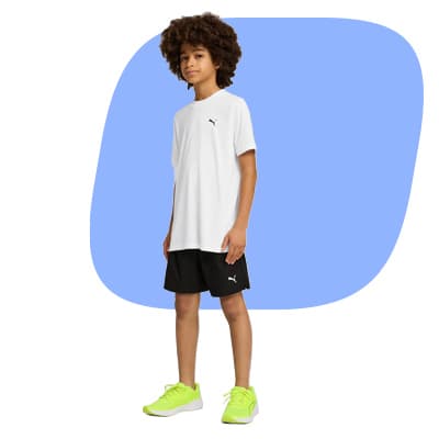 Junge steht seitlich in weißem T‑Shirt, schwarzen Shorts und neonfarbenen Sportschuhen vor hellblauem Hintergrund