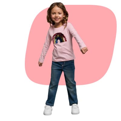 Kind mit langen Haaren in rosa Shirt mit Regenbogenmotiv und Jeans steht lächelnd vor rosa Hintergrund