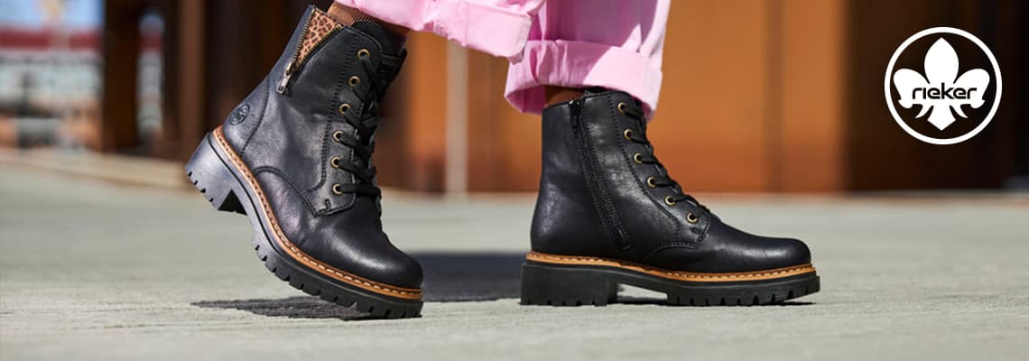 Person in blauen Jeans trägt braune Rieker-Stiefeletten mit heller Sohle und seitlichem Stretch auf grauem Gehweg