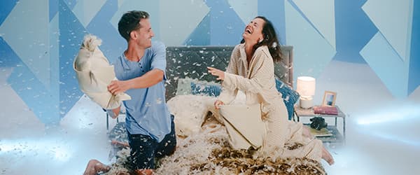 Frau in weißem Pullover hält geöffneten Geschenkkarton und Parfümflasche, umgeben von bunt verpackten Geschenken