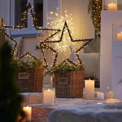 Weihnachtliche Dekoration mit leuchtenden Sternen, Kerzen und Körben auf einer Treppe, im Hintergrund Lichterketten.