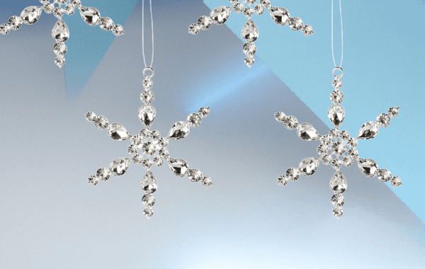 Glitzernde Schneeflocken-Anhänger mit Kristallen vor blau-weissem Hintergrund, an dünnen Fäden hängend