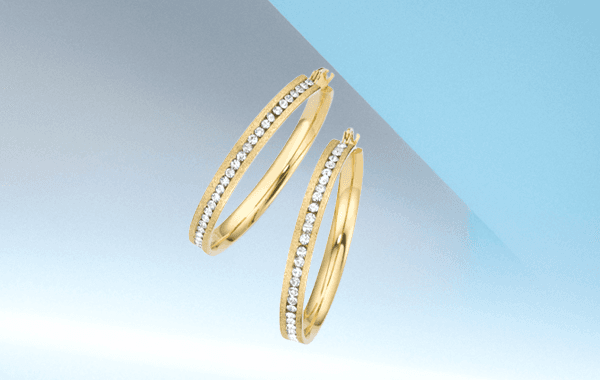 Zwei goldene Creolen mit glitzernden Steinen, vor einem blau-grauen Hintergrund schwebend