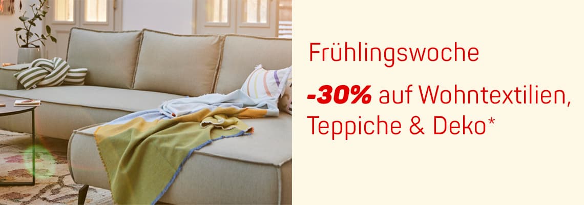 -30% auf Wohntextilien, Teppiche & Deko – Beige Sofa mit bunten Decken, Kissen und Pflanzen im Hintergrund